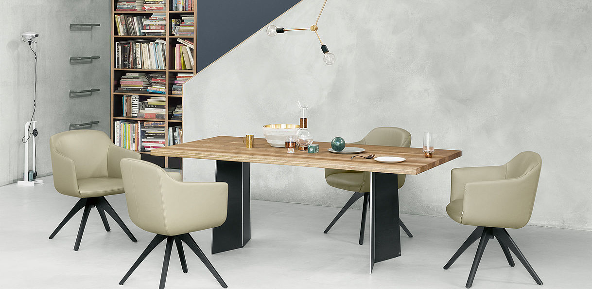 Esszimmer mit modernem Holztisch, vier beigen Stühlen, Bücherregal im Hintergrund und stilvoller Beleuchtung