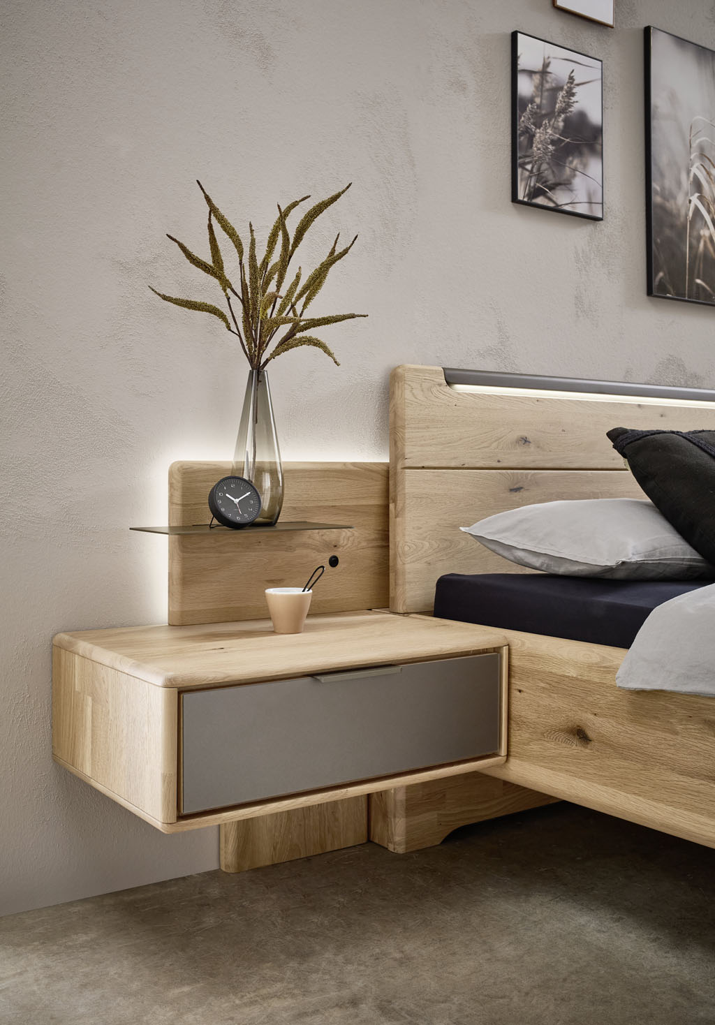 Nahaufnahme eines Holzbettes mit einer Hängekonsole mit braucher Schubladenfront und Paneelaufsatz mit Beleuchtung stilvoll dekoriert