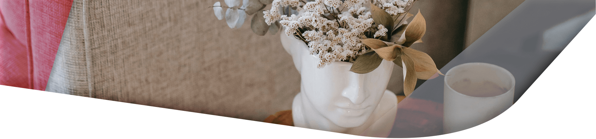 Weiße Büste als Blumenvase mit Trockenblumen arrangiert, neben einer Kaffeetasse auf einem Tisch.