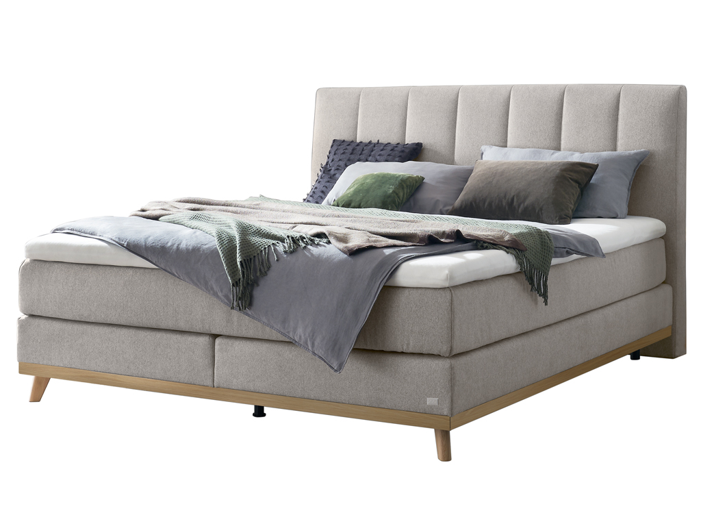 Ein freigestelltes Produktfoto des Hasena Boxspringbettes Pronto Stefania mit einem hellgrauen Stoffbezug, dekoriert mit Kissen und einer Decke.