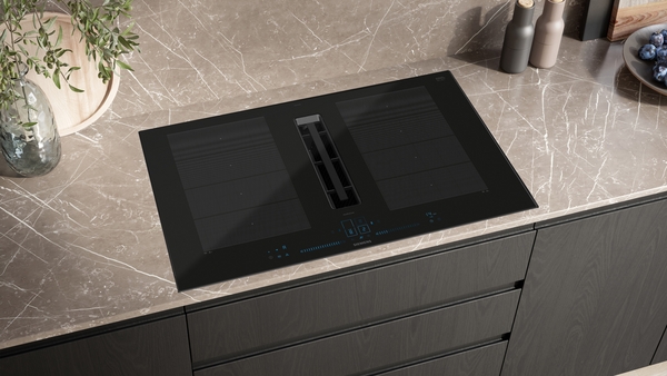 Schwarze Kochplatte mit integriertem Dunstabzug auf marmorierter Küchenarbeitsfläche, umgeben von Dekoration und Küchenutensilien