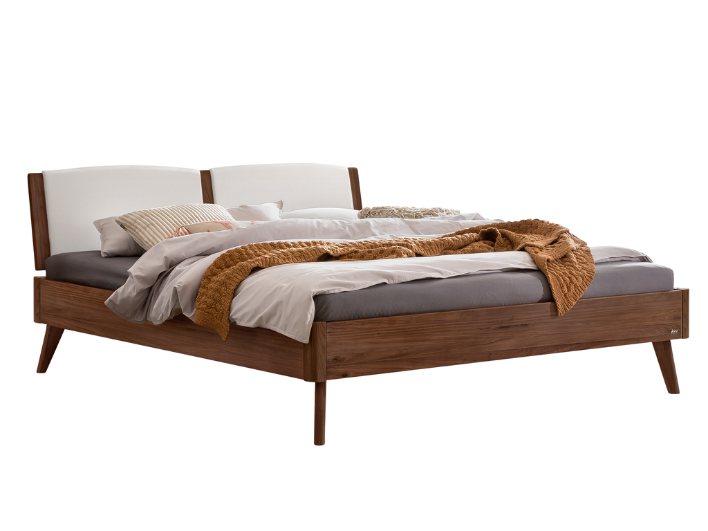 Ein modernes Doppelbett mit einem Bettgestell aus dunklem Walnussholz und einem geteilten, weißen, gepolsterten Kopfteil. Es ist mit einer braunen Strickdecke und verschiedenen beigen und grauen Bettwaren drapiert. Die Beine sind konisch zulaufend.