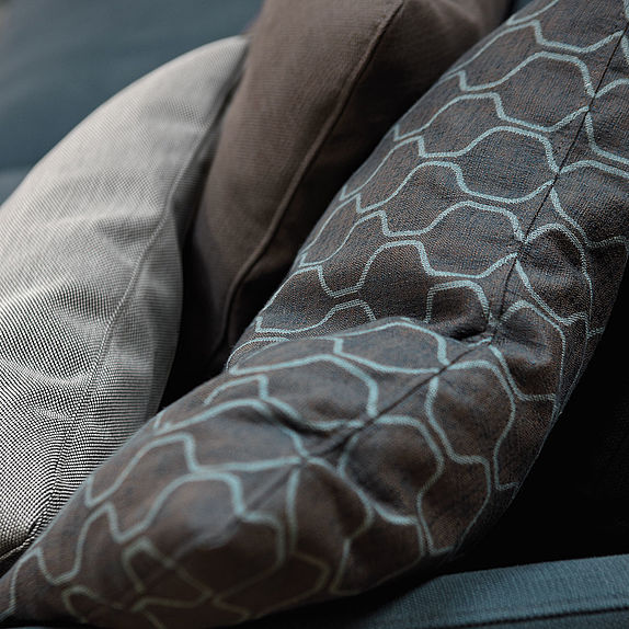 Drei dekorative Kissen in verschiedenen Brauntönen und Mustern auf einem Sofa