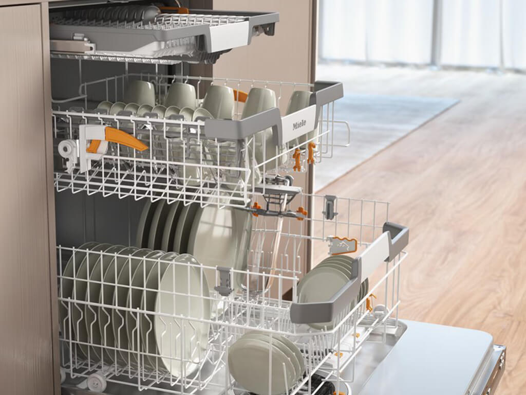 Innenansicht eines geöffneten Miele Geschirrspülers, beladen mit Tellern, Tassen, Gläsern und Besteck in den oberen und unteren Körben.