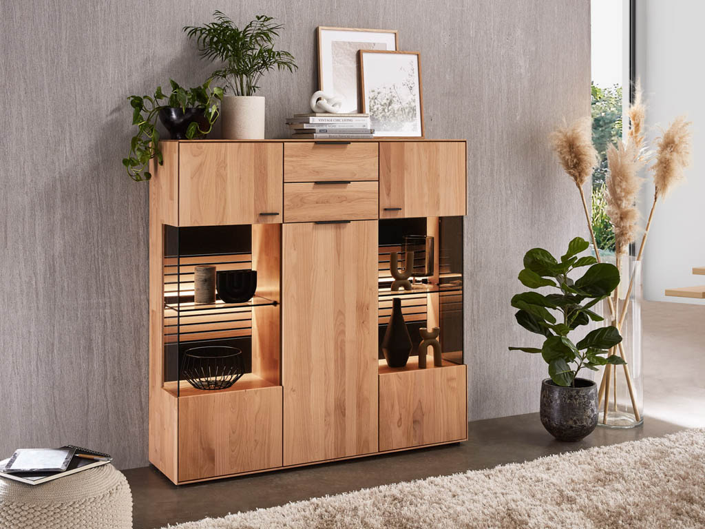 Wöstmann WM 2320 - Highboard  | B: 136,9 cm | Type 4340 Ein stilvolles Holzsideboard in einem modernen Raum, dekoriert mit Pflanzen und Accessoires, integriertem Licht und dekorativen Gegenständen im Inneren