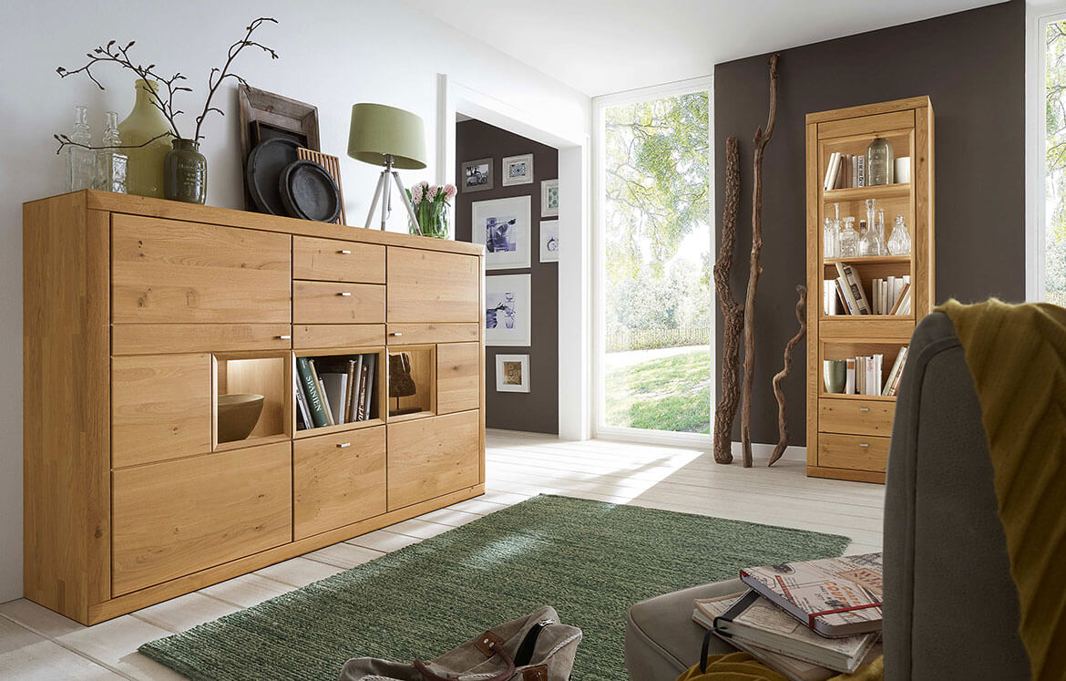 Wöstmann Aurum - Highboard mit offenem Fach | Type 3841/3041 | Wildeiche massiv | konfigurierbar Wohnzimmer mit Holzkommode und Regal, dekoriert mit Vasen und Lampe, offener Raum mit Blick ins Grüne.