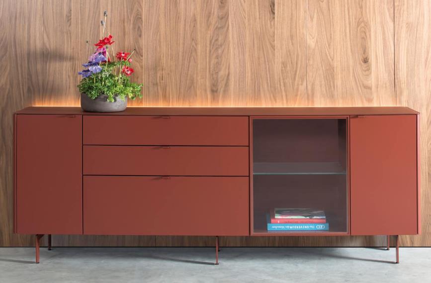 Sudbrock Goya - Sideboard | 3 Türen, 3 Schubladen | Glattlack ziegelrot | B: 245,2 cm Rotes Holz-Sideboard mit Schubladen, Glastür und Dekoration, an einer Holzwand im Wohnzimmer platziert