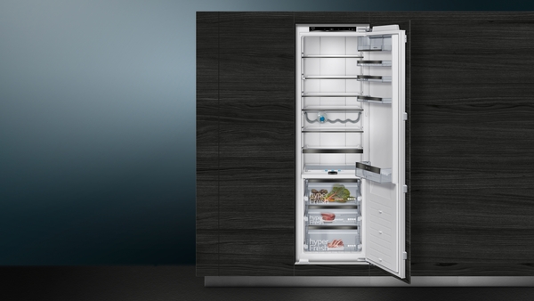 Ein eingebauter Kühlschrank mit geöffneter Tür zeigt mehrere Ablagefächer und ein geräumiges Inneres in einer stilvollen, dunklen Küchenumgebung.