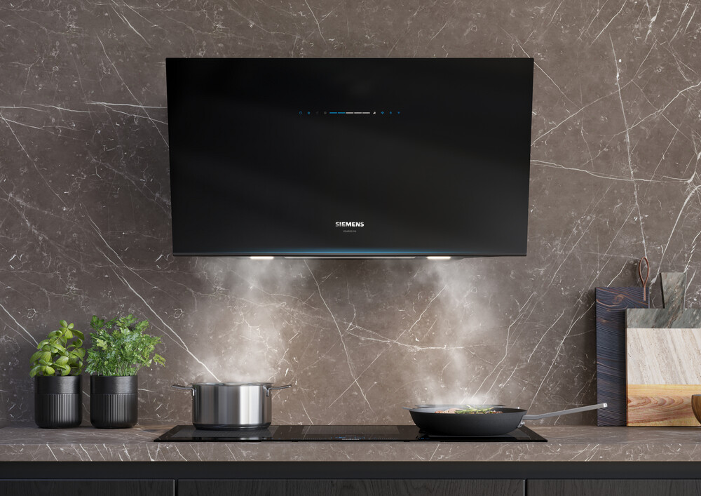 Moderne Dunstabzugshaube über einem Induktionskochfeld mit dampfendem Kochtopf und Pfanne in stilvollem Küchenambiente