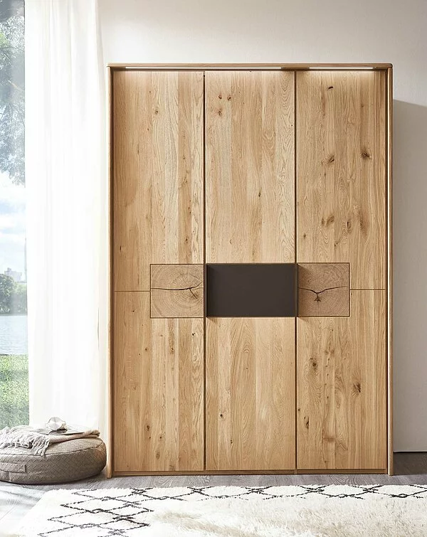 Wöstmann WSM 1600 - Kleiderschrank | Wildeiche massiv | Hirnholzakzent | alle Breiten konfigurierbar Holzkleiderschrank mit natürlicher Maserung und schlichtem Design in einem hellen Raum