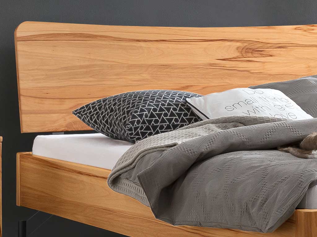 Ausschnitt von einem braunem Holzbett mit Holzkopfteil und moderner Bettwäsche Hasena
