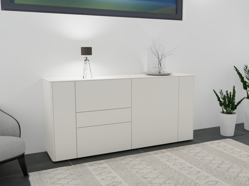 Weiße Kommode mit Schubladen, Tischlampe und Dekoelementen auf einem Teppich.