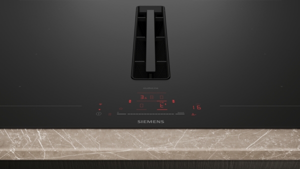 Nahaufnahme der Mitte des Induktionskochfelds. Man sieht die Steuerung des Abzugs und des Kochfelds mit roter Digitalanzeige und Touch-Bedienung. Der integrierte Dunstabzugsschacht ist zentral positioniert.