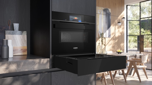 Eingebauter Siemens StudioLine Backofen mit Touch-Display über einer teils geöffneten, schwarzen Schublade (Dampfschublade) in einer modernen Küche. Die Schublade ist bis zur Hälfte herausgezogen und die obere Klappe ist geschlossen.