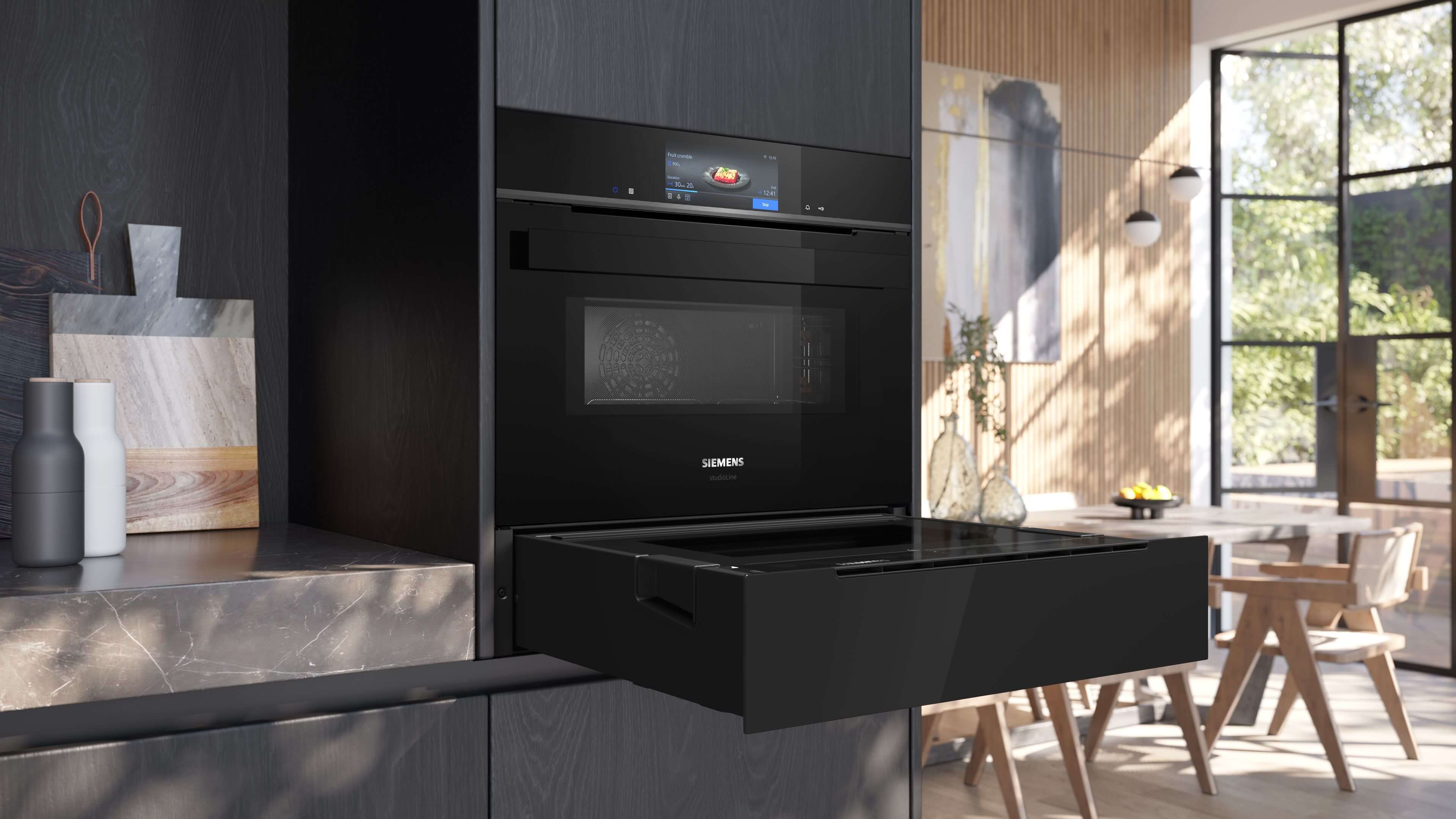 Eingebauter Siemens StudioLine Backofen mit Touch-Display über einer teils geöffneten, schwarzen Schublade (Dampfschublade) in einer modernen Küche. Die Schublade ist bis zur Hälfte herausgezogen und die obere Klappe ist geschlossen.
