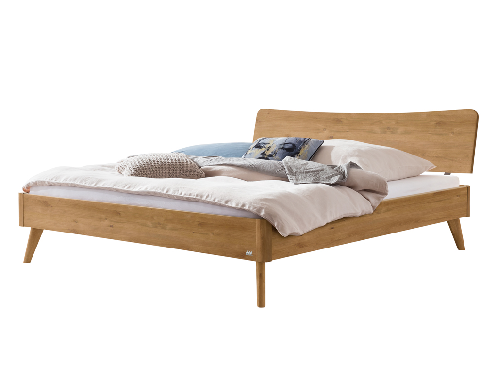 Ein freigestelltes Hasena Bett Caluso aus natur geölter Wildeiche. Das Bett hat ein geschwungenes Kopfteil, schräg ausgestellte Beine und ist mit Kissen und einer Decke dekoriert.