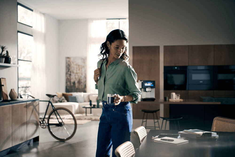 Eine Frau in lässiger Kleidung hält eine Tasse Kaffee in einem modernen Wohnzimmer mit einem Fahrrad im Hintergrund.