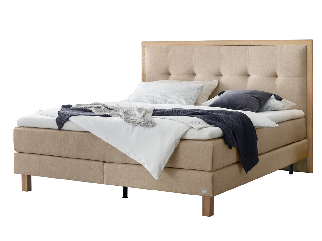 Ein freigestelltes Produktfoto des Boxspringbettes Hasena Pronto Solara in Beige, dekoriert mit Decken und Kissen.