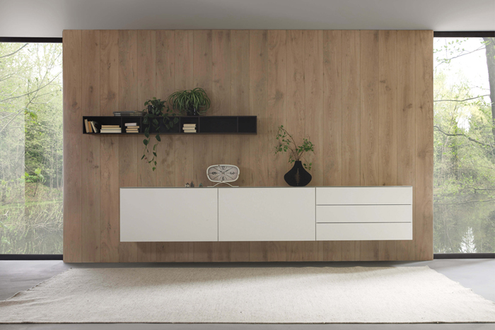 Sudbrock Cubo - Sideboard mit Hängeelement | B: 340 cm variabel | Eiche anthrazit furniert, Lack verkehrsweiß Schlichtes, modernes Wohnzimmer mit einem weißen Schrank und einem schwarzen Regal an einer Holzvertäfelung. Dekoration mit Büchern und Pflanzen.