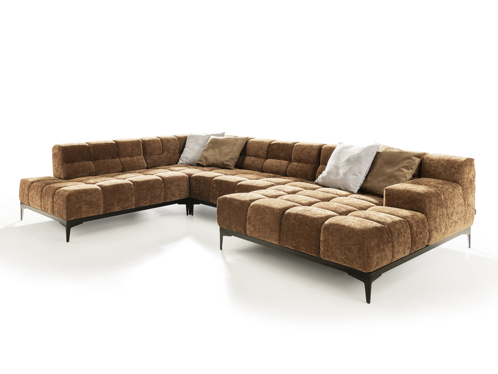 Ein großes, modulares Ecksofa in U-Form, bezogen mit einem braunen, texturierten Stoff mit gestepptem Muster. Das Sofa steht auf eleganten schwarzen Metallfüßen und ist mit vier Zierkissen in Hellgrau und Beige ausgestattet. Der Hintergrund ist weiß.