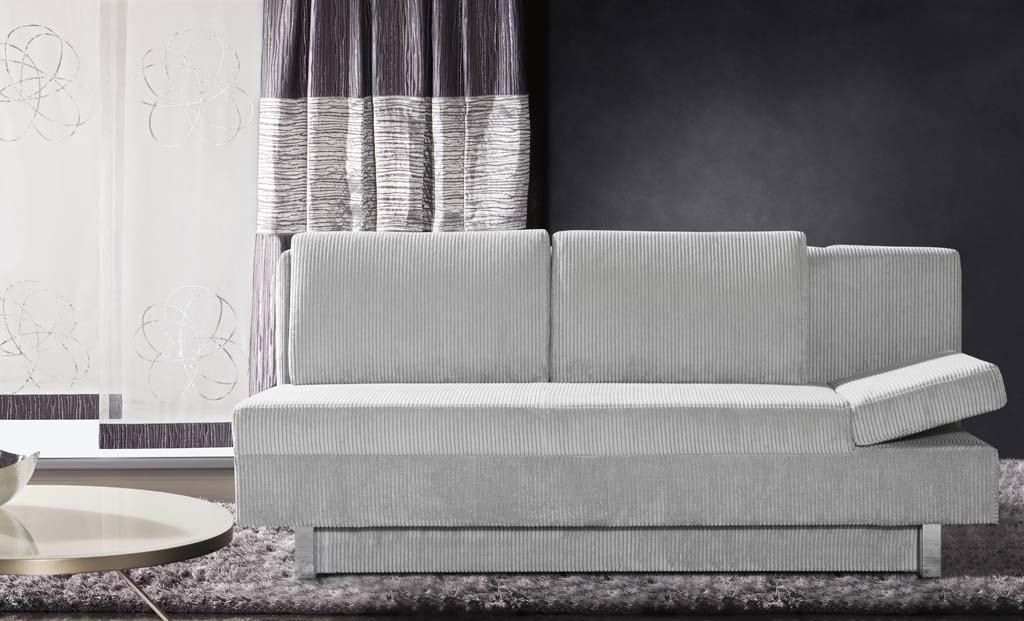 Restyl Tino - Schlafsofa (Querschläfer) | hellgrau | mit Bettkasten | 150 x 200 cm Ein stilvolles graues Sofa in einem modern eingerichteten Wohnzimmer, das vor dunklen Wänden mit gemusterten Vorhängen steht.