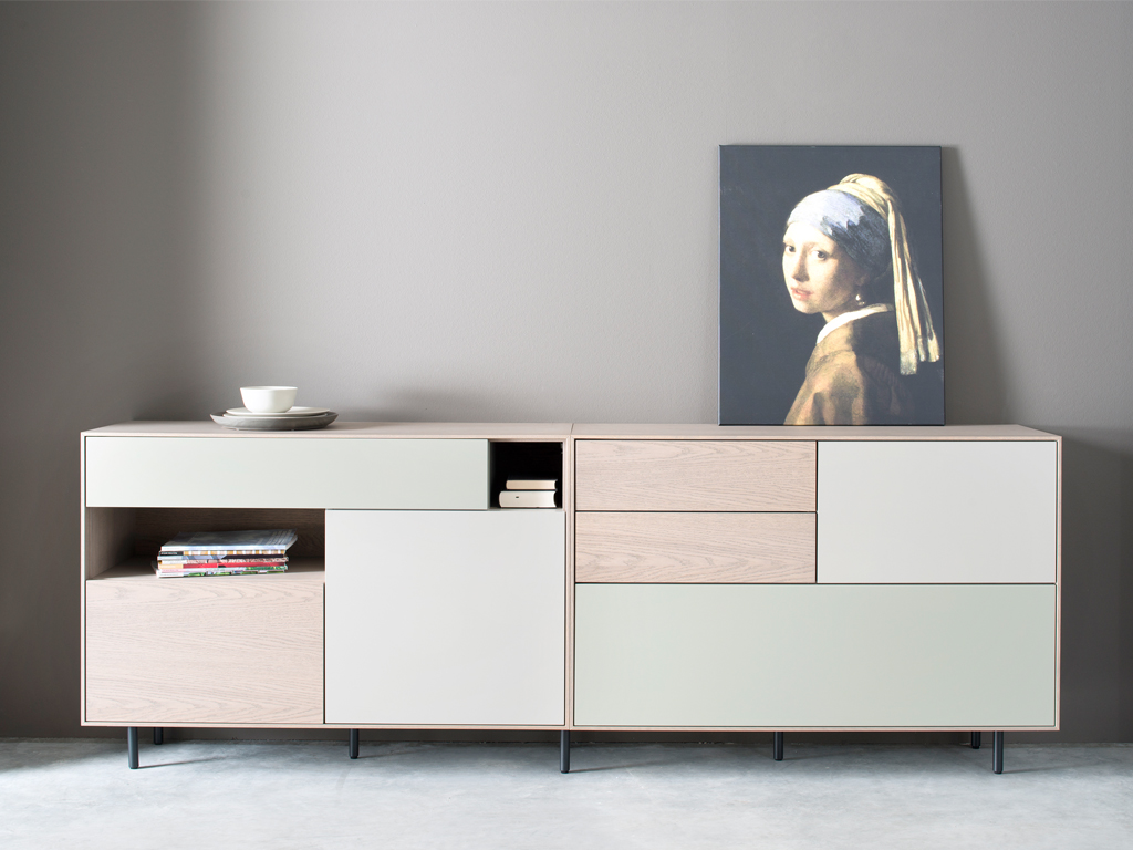 Sudbrock Game - Sideboard | Eiche sahara furniert, Lack salbei, Lack muschelgrau | B: 240 cm Helle Kommode mit modernen Schubladen und darauf stehendem Kunstwerk, daneben ein Stapel Bücher und ein Teller mit Schale