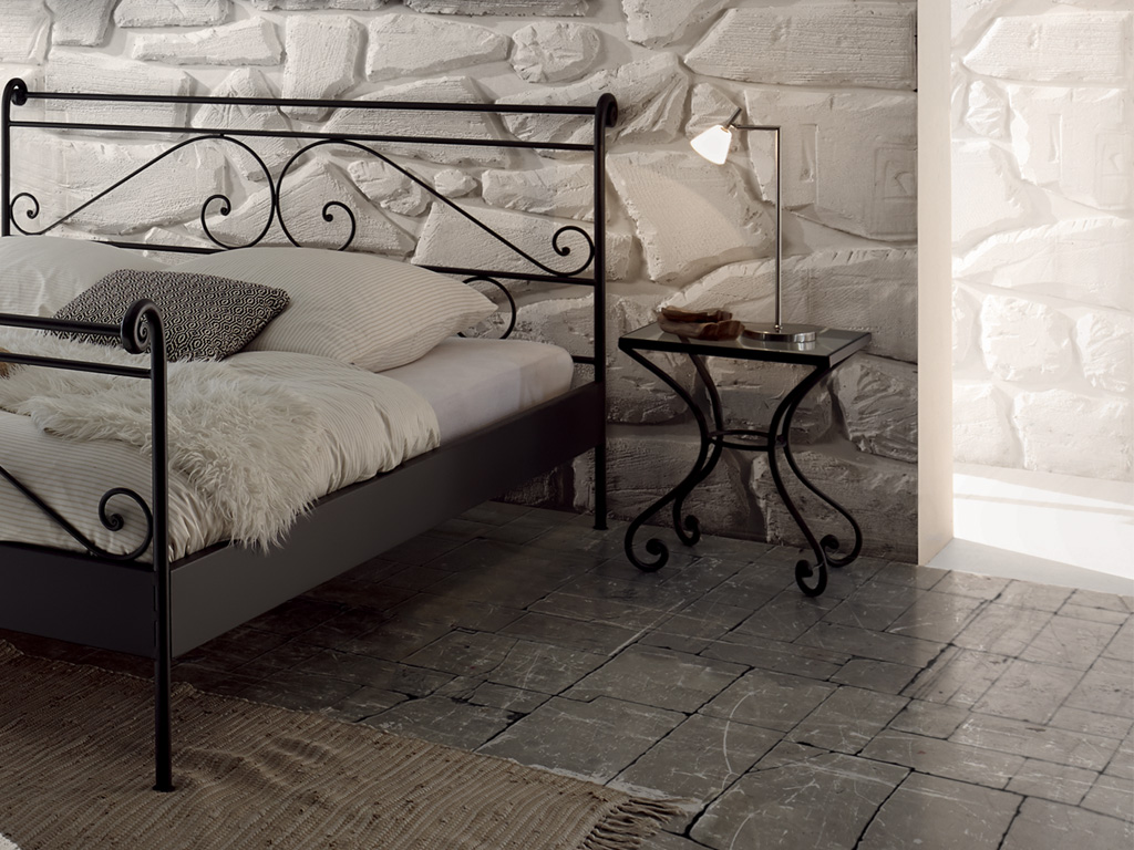 schwarzer Nachttisch auf filigranem Eisenmetallgestell mit Glasplatte an einem Metallbett mit weißer Bettwäsche in einem stilvollen Zimmer Cura von Hasena