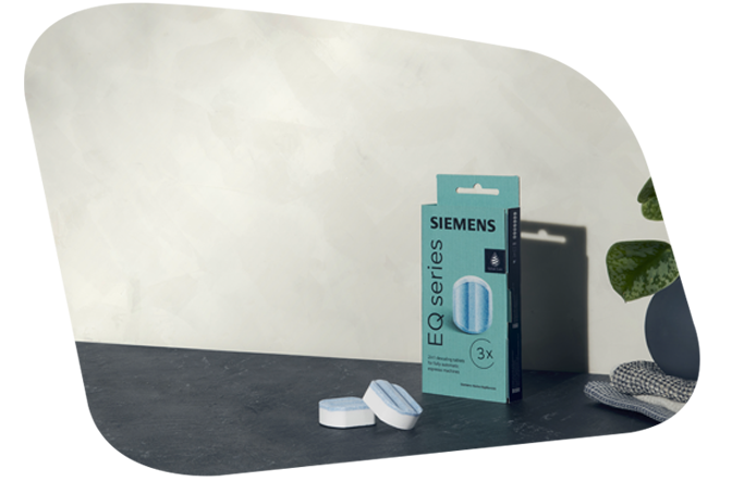 Nahaufnahme einer Packung Siemens EQ series Entkalkungstabletten (3x) und zwei lose liegenden Tabletten auf einer dunklen Arbeitsfläche vor einer hellen, strukturierten Wand.