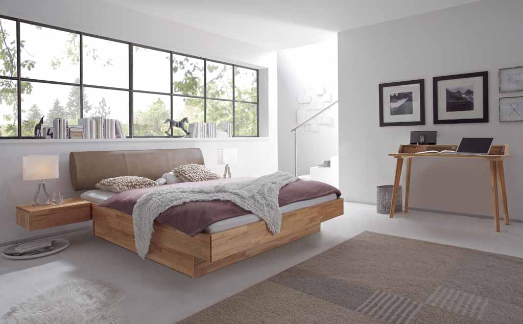 Ein helles Schlafzimmer mit einem modernen Holzbett, großen Fenstern, einem Schreibtisch und neutralen Farbtönen.