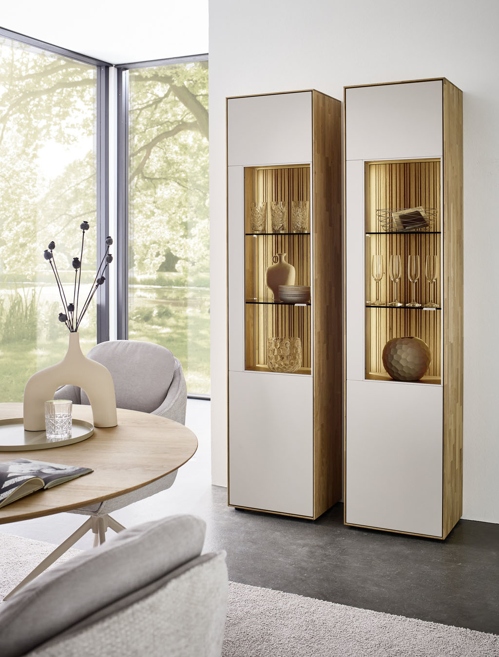 zwei moderne große Vitrinenschränke mit Beleuchtung in braun-weiß und Glasausschnitt stilvoll dekoriert in einem hellen Raum