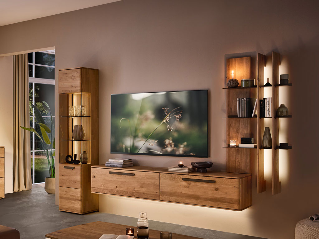 moderne Wohnwand aus Eiche mit einem beleuchtetem Hängelowboard, Aufsatzregal und Standvitrine stilvoll dekoriert in einem modernem Zimmer