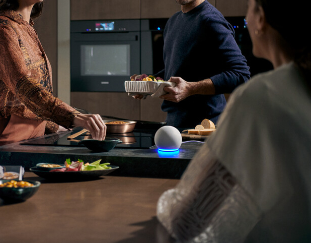 Drei Personen in einer modernen Küche, die einen intelligenten Lautsprecher auf der Arbeitsplatte verwenden