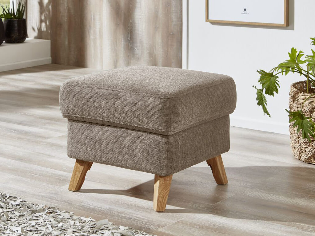 sit&more Freiburg | Hocker | 6020/6028 Ein brauner Polsterhocker mit Holzbeinen steht auf einem Holzboden in einem modern eingerichteten Wohnzimmer.