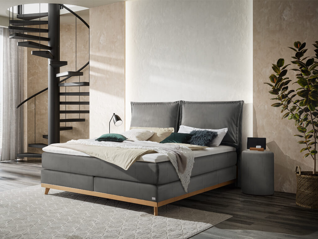 Boxspringbett Hasena Pronto Imelda in Stahlgrau mit einem Holzfußgestell aus geölter Eiche in einem modern eingerichteten Schlafzimmer.