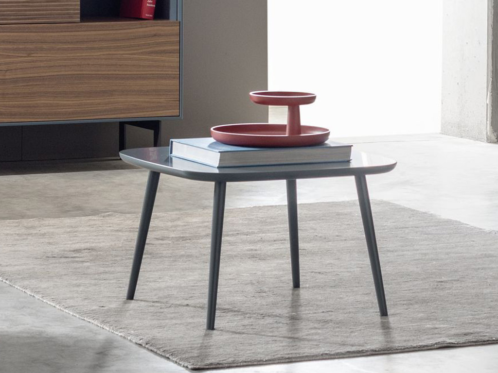 Sudbrock Mellini - Couchtisch quadratisch 60 cm | Massivholz oder Lackausführung | Höhe 39 oder 49 cm Ein stilvoller, moderner Couchtisch mit Büchern und einer roten Schale als Dekoration, platziert auf einem Teppich im Wohnzimmer.