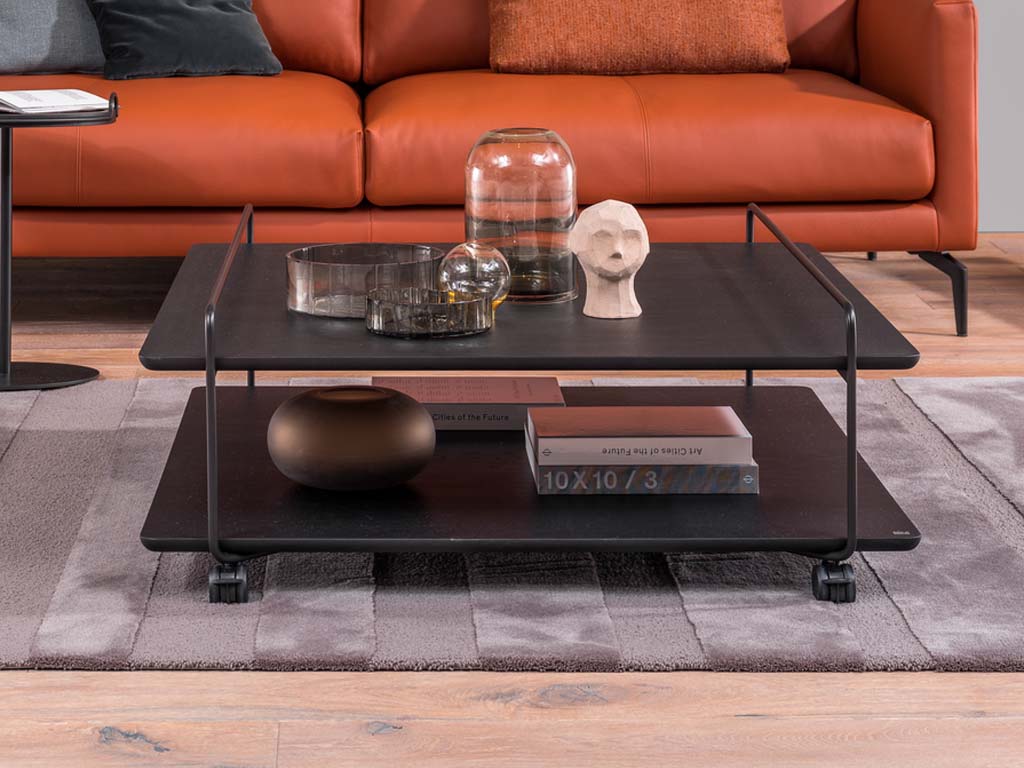 Rolf Benz 931 - Couchtisch auf Rollen | Eiche schwarz | 102 x 100 cm Couchtisch in schwarz mit Rollen vor einer rot/orangen Couch