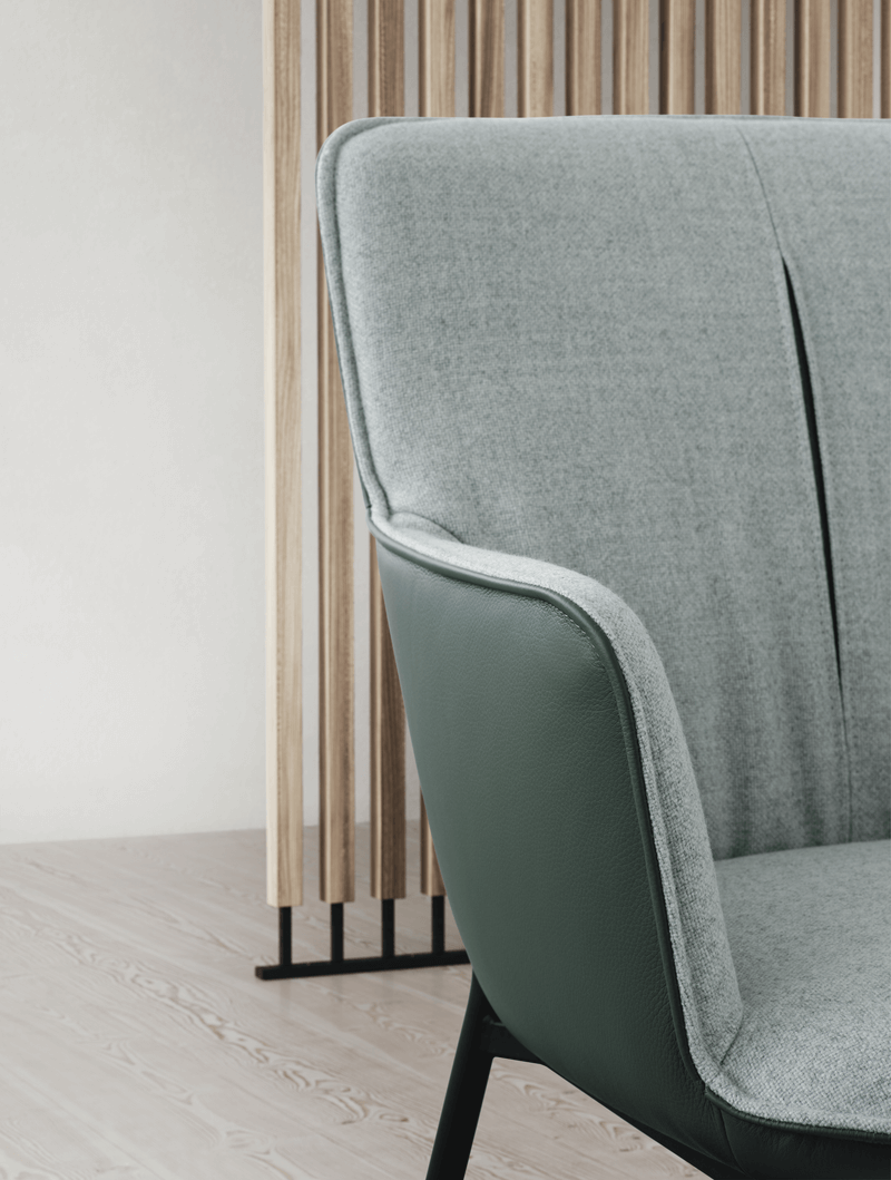 Seitliche Nahaufnahme eines modernen Sofas mit grauem Stoff und grüner Lederverkleidung in einem minimalistischen Raum