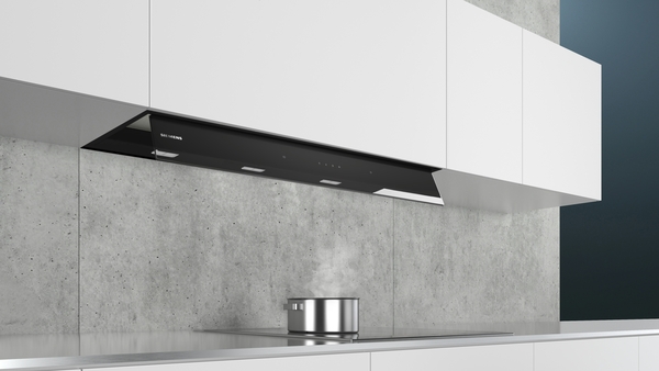 Eine moderne Dunstabzugshaube in einer eleganten, minimalistischen Küche über einem Kochfeld mit dampfendem Topf.