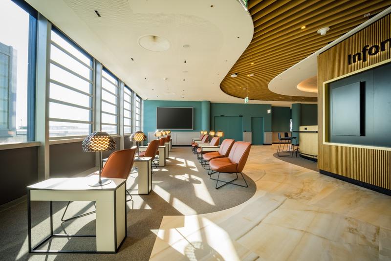 Ein lichtdurchfluteter Warteraum mit modernen Sesseln, Holzelementen und großen Fenstern.