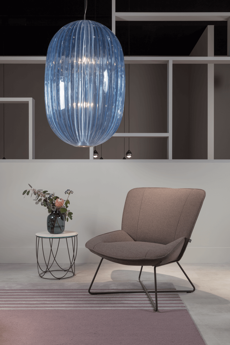 Ein gemütlicher Wohnbereich mit einem braunen Sessel, einem runden Beistelltisch mit Vase und einer großen, blauen Pendelleuchte.