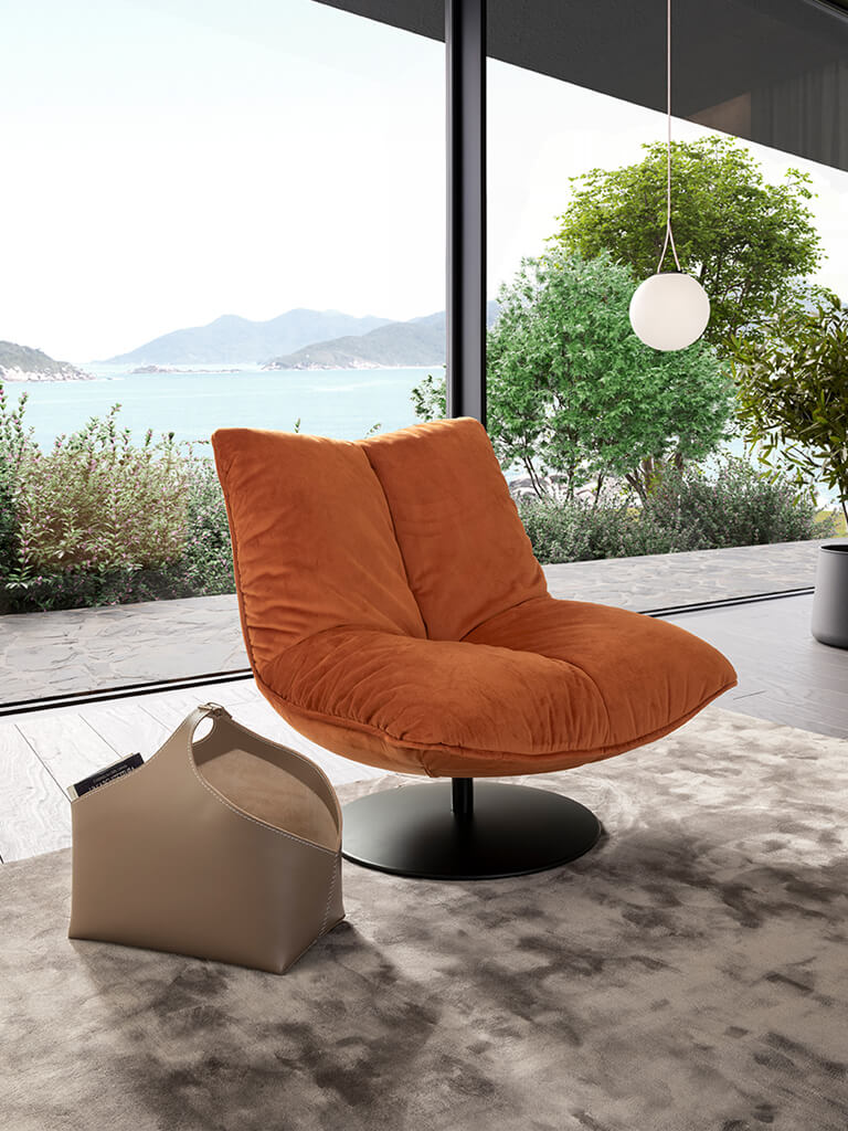 Ein gemütlicher, orangefarbener Sessel steht vor einem großen Fenster mit Blick auf einen See und Berge, neben einem hellen Teppich und einer modernen, hängenden Leuchte.