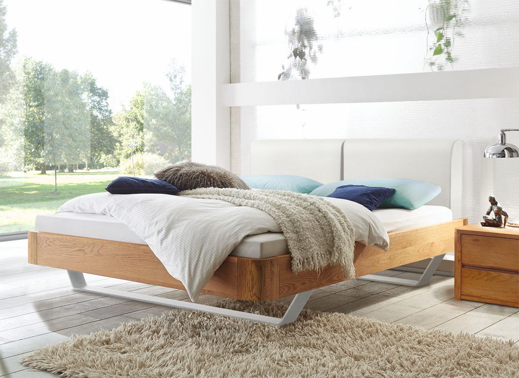 Modernes Bett mit braunem Rahmen und weißen Kufen und einem weißen Polsterkopfteil mit braunem Nachtschrank mit Schubladen stilvoll dekoriert in einem modernen Zimmer