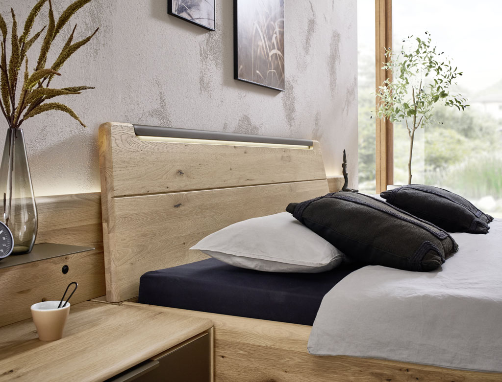 Detailaufnahme eines modernen Holzbettes mit Beleuchtung am Kopfteil stilvoll dekoriert