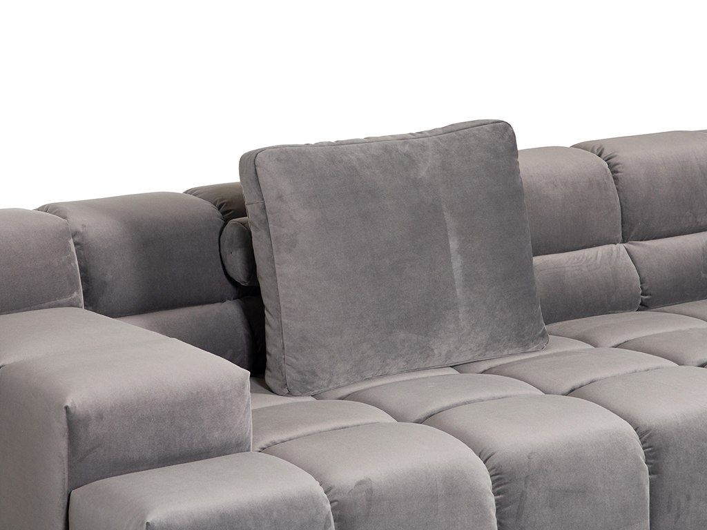 Nahaufnahme eines hellgrauen Samtsofas. Ein quadratisches Rückenkissen aus demselben Stoff ist in die Rückenlehne des Sofas eingesetzt. Die Sofapolsterung hat ein gestepptes, quadratisches Muster.