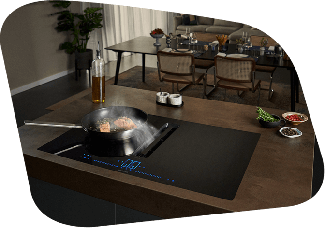 Elegante Küche mit Kochfeld, auf dem ein Gericht zubereitet wird. Im Hintergrund ein Esstisch mit gedeckten Plätzen.