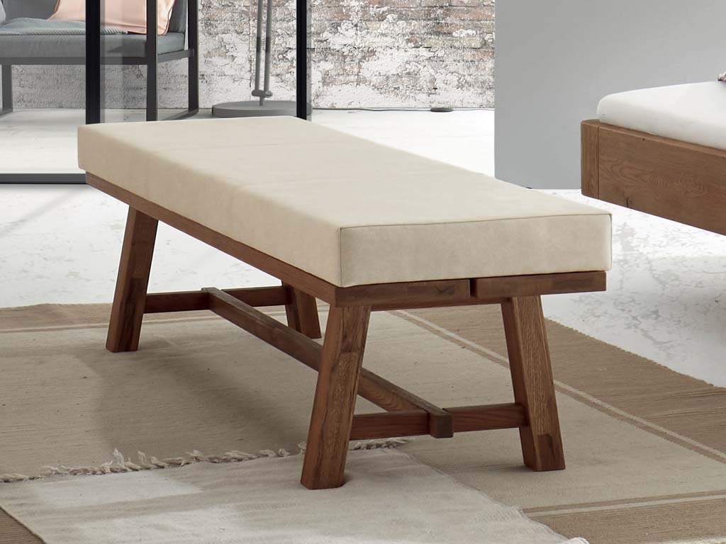 stilvolle Holzbank aus Nussbaum mit einer dicken Polsterauflage in creme auf drei beigen Teppichen