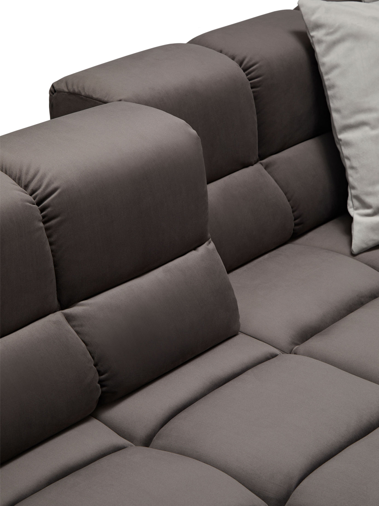 Nahaufnahme des dunkelgrauen Sofas mit gestepptem Muster. Der Fokus liegt auf der Verbindung zwischen Sitzfläche und Rückenlehne, die ebenfalls aus einzelnen Polstersegmenten besteht. Ein hellgraues Kissen ist oben rechts sichtbar.
