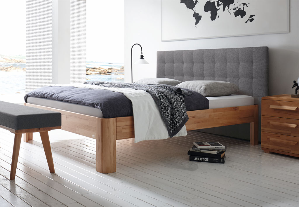 modernes Bett mit braunem Rahmen und braunen Füßen sowie eine Wandpaneel aus Polster in grau mit passender Bettbank und Nachtschrank stilvoll dekoriert in einem modernen Zimmer