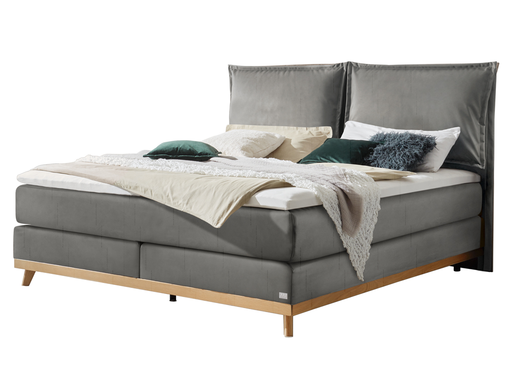 Ein modernes Boxspringbett in Dunkelgrau mit einem gepolsterten Kopfteil und Holzfüßen, stilvoll dekoriert mit Kissen und einer Decke auf weißem Hintergrund.