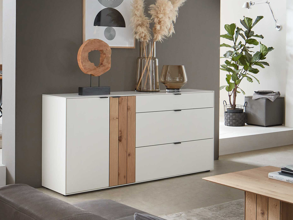 Wöstmann WM 2380 - Sideboard | Type 2853/2854 | B: 181,9 cm | Lack, Balkeneiche-Akzent | konfigurierbar Ein stilvolles Wohnzimmer mit einer modernen weißen Kommode, dekoriert mit Holzelementen, einer Vase und einem Kunstobjekt, umgeben von einer Pflanze und weiteren Dekorelementen.